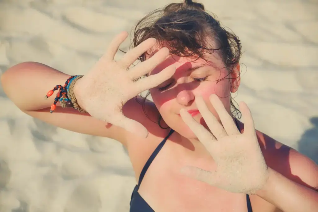 A woman applying sunscreen on her face and arms outdoors on a sunny day